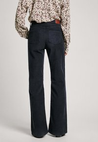 Tmavěmodré manšestrové kalhoty s rozšířenými nohavicemi a strukturovaným povrchem, s dvěma zadními kapsami a hnědou koženou nášivkou na pásku.