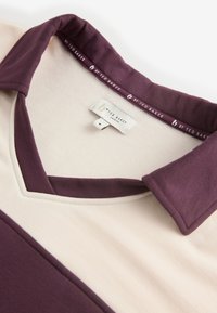 Kleurvlakken polo met een diepe violette kraag, crèmekleurig lichaam en een V-hals ontwerp. Heeft een stoffen label met de tekst "by Ted Baker."
