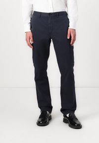 Marineblauwe katoenen cargo-broek met een rechte pijpdesign, voorzien van zijzakken en een knoopsluiting. G gedragen met zwarte leren schoenen.