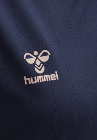 Navyblå ribbad tyg med ljusbeige hummel-logotyp som har en stiliserad bumblebee ovanför varumärket.