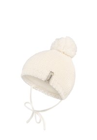 White knitted baby hat with pom-pom, ear flaps, and tied chin straps, featuring a small fabric label on the front edge.