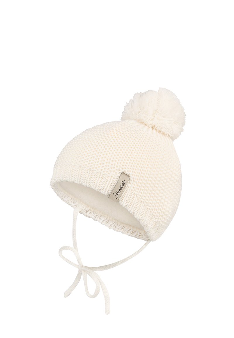 White knitted baby hat with pom-pom, ear flaps, and tied chin straps, featuring a small fabric label on the front edge.