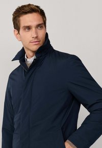 Dunkelblaues Jackett mit hohem Kragen, Reißverschluss und Seitentaschen. Glatte Textur mit einem eleganten, modernen Design.