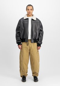 Svart skinn bomberjakke med en beige saueskinnskrage, worn over en hvit T-skjorte og løse khaki cargo bukser, kombinert med svarte sko.