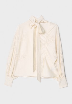 Cremefarvet bluse med knyttet krave, lange pufærmer og teksturerede blomster mønstre på stoffet. Blødt, let materiale.