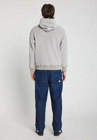 Hoodie gris avec une grande capuche, des poignets et un ourlet côtelés, associé à un jean bleu foncé ample avec deux poches arrière. Design simple.