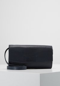 Námořnická kožená crossbody taška s texturovaným povrchem, klopovým uzávěrem a odnímatelným popruhem; na přední straně se nachází diskrétní logo.