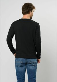 Schwarzes langärmeliges Hemd mit Rundhalsausschnitt, kombiniert mit blauen Jeans aus Denim mit Gesäßtaschen und einem leichten Verblassen. Rückansicht.