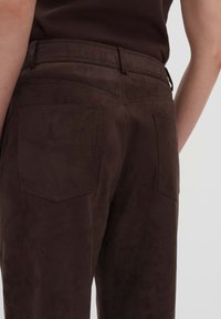 Braune Wildlederhose mit glatter Textur, einem taillierten Bund und zwei Gesäßtaschen mit rechteckigen Klappen.