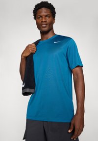 Blå atletisk skjorte med korte ærmer, Nike-logo på venstre skulder, parret med et mørkt håndklæde hængende over den ene skulder.