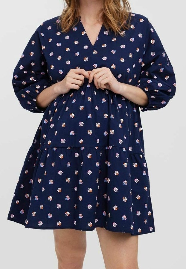 Laivansininen mekko, jossa on V-mallinen kaula-aukko, lyhyet puffihihat ja kerroksellinen muotoilu. Kaikissa kankaissa on vaaleanpunaisia ja valkoisia kukkakuoseja.