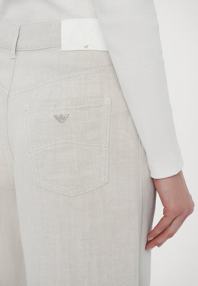 Light gray denim jeans feature a back pocket with silver hardware and a white label. The texture appears soft with a smooth finish.