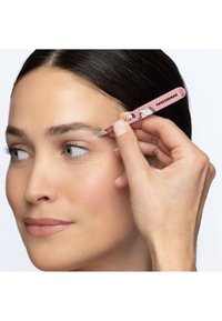 Kvinna som håller rosa Tweezerman-pincett med tecknade motiv och formar sitt vänstra ögonbryn mot en vit bakgrund.