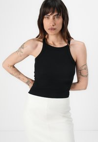 Svart ribbete tank topp med høy hals og tynne stropper, sammen med et tettsittende hvitt skjørt. Tatovering synlig på armen.