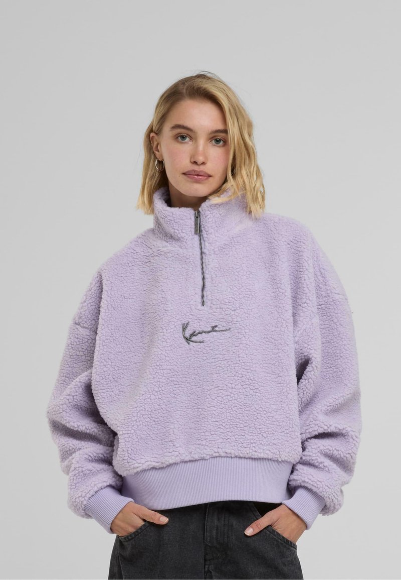 Licht paarse fleece pullover met hoge kraag, halve rits aan de voorkant en geribbelde zoom. Bevat geborduurde details op de borst. Zachte textuur.