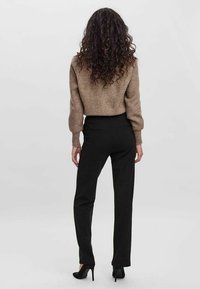 Pull en texture marron associé à un pantalon noir ajusté et des chaussures à talons hauts. Vue de dos, mettant en valeur l'ajustement et la silhouette de la tenue.
