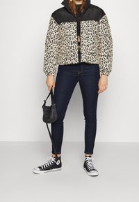 Pälsmönstrad puffjacka med svart överdel, dragkedja och elastiska ärmmuddar, i kombination med mörka smala jeans och svarta sneakers. Liten svart väska.