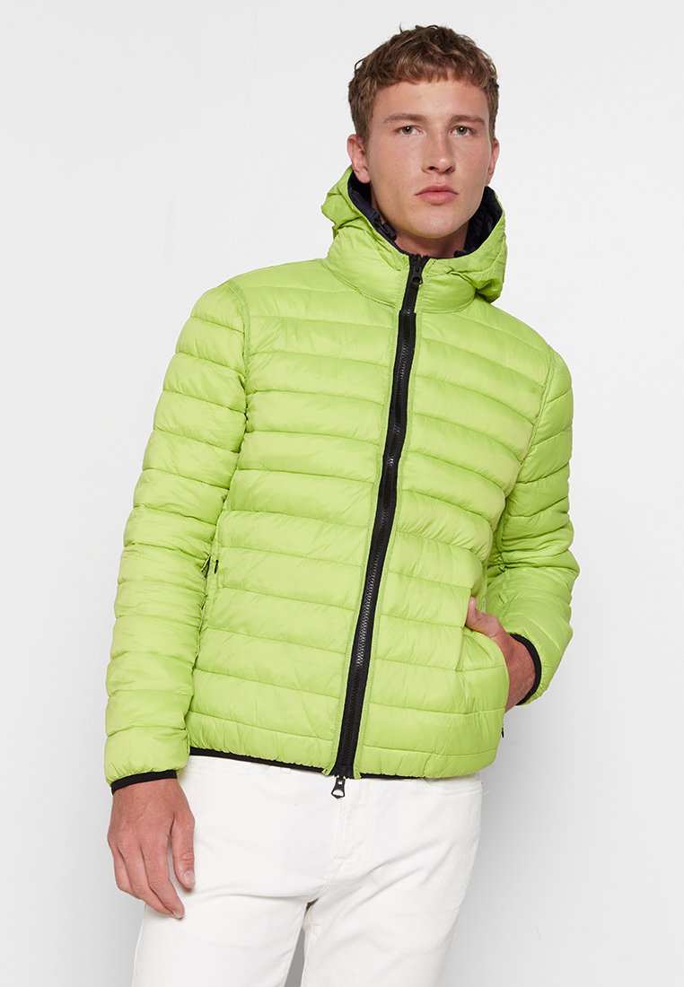 Lichtgroene pufferjack met horizontale stiksels, ritssluiting en capuchon. Beschikt over twee zijzakken en zwarte ritssluitingaccenten. Lichtgewicht materiaal.
