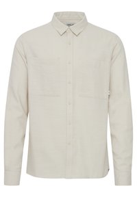 Camisa de manga larga en color beige claro con un tejido texturizado, que cuenta con un cuello desplegado, dos bolsillos en el pecho y cierre de botones en la parte delantera.