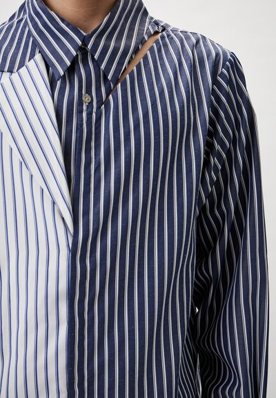 Gestreiftes Hemd mit Knopfleiste, das abwechselnd navyblaue und weiße vertikale Streifen zeigt, mit einem Cut-Out-Detail am Kragen und einem lässigen Schnitt.