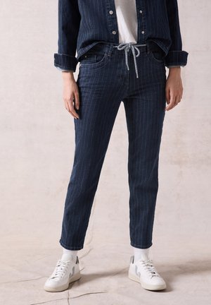 Donkerblauwe spijkerbroek van denim met een streeppatroon, voorzien van een trekkoord in de taille en zijzakken, gecombineerd met witte sneakers en sokken.