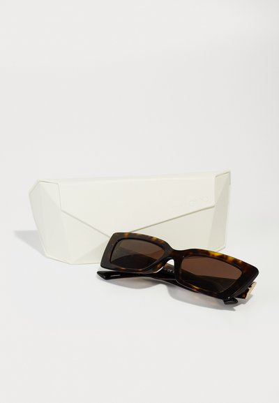 Lunettes de soleil en écaille de tortue avec des montures rectangulaires arrondies et des verres marron, accompagnées d'un étui géométrique blanc.