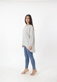 Lichtgrijze, oversized trui met een afgeronde zoom, lange mouwen en geribbelde manchetten, gecombineerd met blauwe skinny jeans en transparante haksandalen.