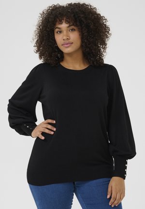 Black knitted sweater with a round neckline, puffed sleeves, and button detailing on the cuffs. Paired with blue jeans.