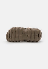 Brown rubber footwear with a textured, ridged surface and ventilation holes. Rounded shape resembling a stylized caterpillar design.