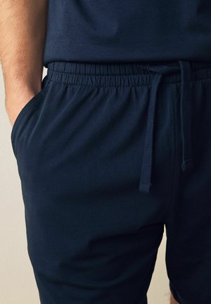 Pantalones cortos azul marino con cintura elástica, cierre de cordón y bolsillos laterales. Tejido suave con un ajuste relajado y sin patrones visibles.