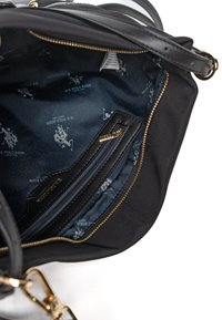 Interior de bolso negro con forro de tela azul marino con el logotipo repetido de U.S. Polo Assn., bolsillo con cremallera y detalle de cremallera en tono dorado.