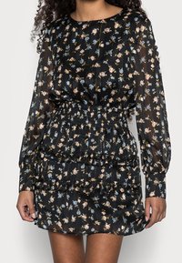 Svart blommig klänning med långa ärmar, med smockad midja och volanger, prydd med små rosa och blå blommönster.