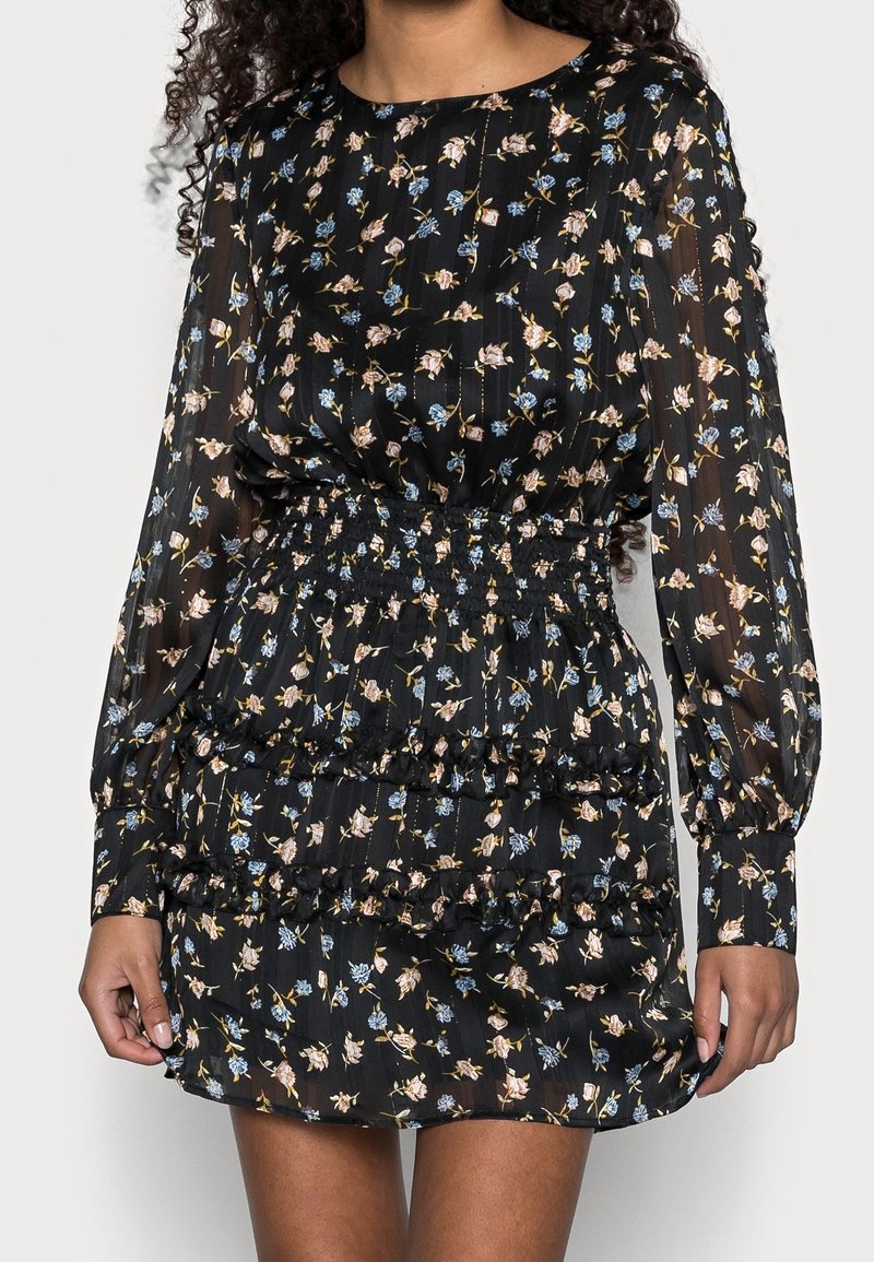 Svart blommig klänning med långa ärmar, med smockad midja och volanger, prydd med små rosa och blå blommönster.