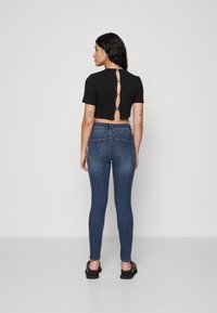 Sort cropped top med åbning på ryggen og knapdetaljer, parret med blå skinny jeans. Glat stof, tætsiddende design og korte ærmer.