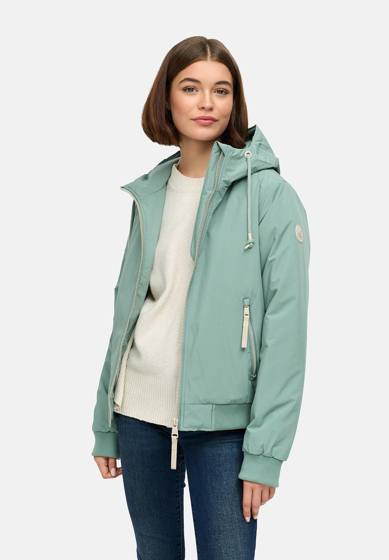 Gaišzaļš jakas ar kapuci, ar rāvējslēdzēju priekšā, kabatām un ribotām aprocēm. Gluds, ūdensnecaurlaidīgs materiāls, stilizēts ar regulējamiem šņorēm.