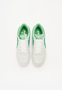 Weiße und grüne Sneakers mit einem perforierten Zehenbereich, Schnürsenkeln und einem gepolsterten Kragen, die kontrastierende grüne Streifen und Branding auf der Zunge aufweisen.