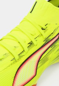 Zapato de fútbol color verde lima con parte superior texturizada, detalles en negro, detalle rojo contrastante y cordones, diseñado para rendimiento y agilidad.