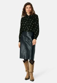 Blusa nera con bottoni e motivo a quadri bianchi. Abbinata a una gonna a matita in pelle scura e stivali morbidi beige.