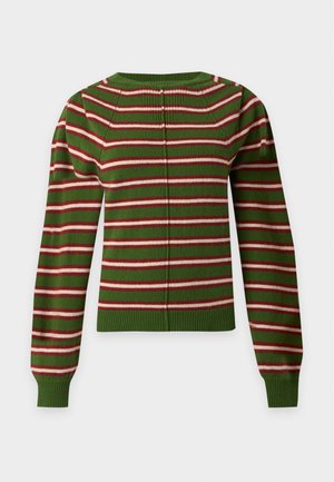 Model iført grønstribet sweater og blå jeans med vide ben med den ene hånd i lommen, stående på en ensfarvet hvid baggrund.