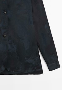 Chemise noire à manches longues avec motif texturé, patte de boutonnage, et ourlet arrondi, confectionnée en tissu léger.