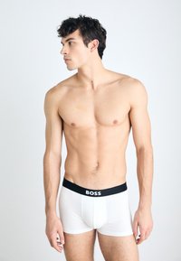 Weiße Boxershorts mit einem schwarzen elastischen Bund, auf dem "BOSS" in weißem Text steht. Der Stoff wirkt glatt und elastisch und sorgt für eine eng anliegende Passform.