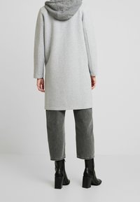 Grijze lange hoodie met een zachte textuur, heeft een contrasterende grijze capuchon en is gecombineerd met grijze cropped broek en zwarte blokhaklaarzen.