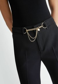 Pantaloni neri con una cintura larga e passanti, caratterizzati da un accento in catena dorata collegato a un anello, che arricchisce il design con texture e brillantezza.