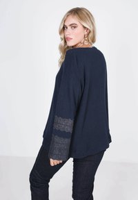 Marine gebreide trui met een gestructureerde stof, voorzien van kantaccenten op de lange mouwen. Relaxte pasvorm met een ronde halslijn en verlaagde schouders.