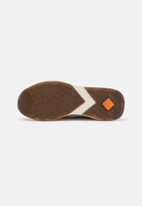Shoe outsole featuring a textured brown rubber surface with a diamond pattern and a white accent stripe. Includes an orange brand logo detail.