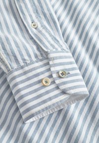 Camicia a righe con strisce orizzontali azzurro chiaro e bianche, colletto con bottoni, bottoni a contrasto con quattro fori e finitura lucida.
