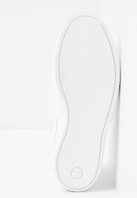 Weiße Sneakersohle aus strukturiertem Gummi, mit abgerundetem Rand und Logodetail an der Ferse. Glatte Oberfläche, minimalistisches Design, klare Linien.