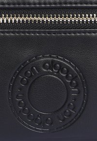 Bolso de cuero negro con un acabado texturizado, cremallera dorada y diseño de logo circular en relieve en la parte frontal.