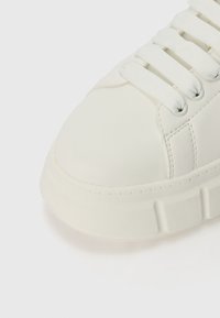 Białe sneakersy z gładką skórzaną cholewką, okrągłym noskiem i płaską gumową podeszwą. Wyróżniają się białymi sznurówkami i subtelnymi detalami szycia.