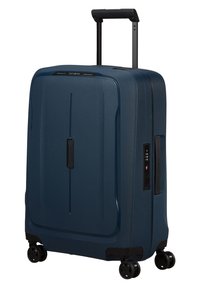 Valise rigide en plastique bleu foncé avec une surface texturée, poignée noire, serrure intégrée et quatre roues noires pour la mobilité.
